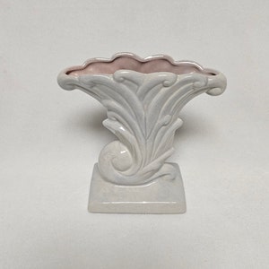 May include: White ceramic vase with a pink interior and a decorative, swirling design. The vase has a square base and a wide, open top.