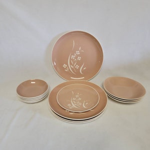 Puede incluir: Un juego de vajilla rosa vintage con diseños florales blancos. El juego incluye platos grandes, platos más pequeños y cuencos. Los platos y cuencos tienen un borde blanco. El diseño floral es un grupo estilizado de flores y hojas.