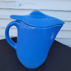 May include: A bright blue ceramic jug with a lid. The jug has a rounded body and a handle. The lid has a unique shape and is designed to pour easily.