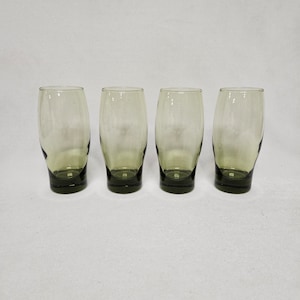 May include: Set of four green glass tumblers. The glasses are clear with a slight green tint and have a rounded, slightly flared shape.