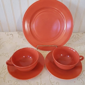 Könnte beinhalten: Ein Set mit orangefarbenen Vintage-Teetassen und Untertassen. Das Set enthält zwei Teetassen und Untertassen sowie einen größeren Teller.
