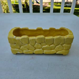 May include: A yellow ceramic planter shaped like a stone wall. The planter is rectangular and has a smooth, glazed finish.