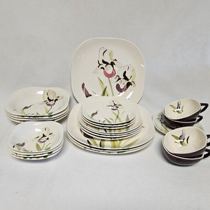 Puede incluir: Un juego de vajilla de cerámica blanca con un diseño floral con iris púrpuras y blancas. El juego incluye una fuente cuadrada grande, un juego de platos para ensalada, un juego de cuencos y un juego de tazas de té.