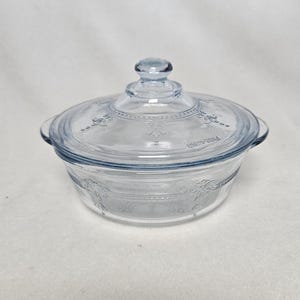 Op de afbeelding: Een doorzichtige glazen schaal met een blauwe tint en een reliëfmotief van bloemen. Het deksel heeft een knop bovenop.