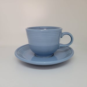 May include: A light blue teacup and saucer set. The cup has a rounded shape and a handle. The saucer has a scalloped edge.