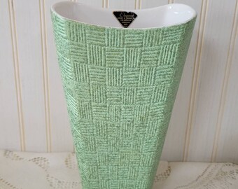 May include: A green ceramic vase with a woven pattern. The vase is tall and slender with a wide mouth. It has a white interior and a label that reads "El Dorado Ceramics, USA".