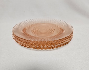 Puede incluir: Una pila de seis platos de postre de vidrio rosa con un borde festoneado.