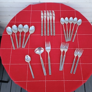 Op de afbeelding: Een set zilveren bestek op een rode tafelkleed. De set bevat lepels, vorken en messen. Het bestek heeft een sierlijk ontwerp.