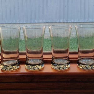 Puede incluir: Cuatro vasos transparentes de vidrio con fondo texturizado, colocados sobre una superficie de madera.