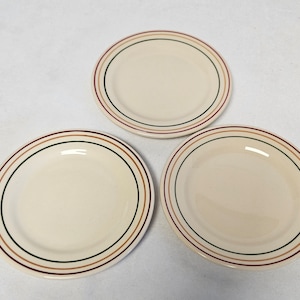 Pode incluir: Três pratos de cerâmica branca com um design de listras marrons, verdes e creme.