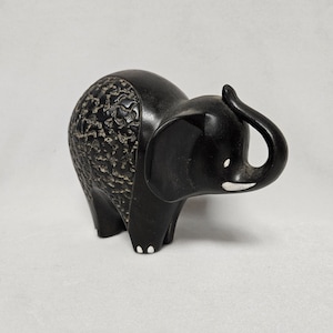 May include: A black ceramic elephant figurine with a textured back and white accents on the trunk and feet.