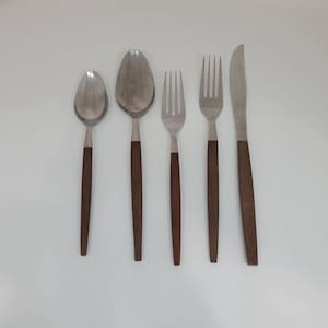 Può includere: Set di cinque posate argentate con manici in legno marrone. Il set comprende un coltello, due forchette e due cucchiai.