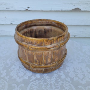 May include: A brown ceramic planter with a bamboo design. The planter is round and has a wide opening.