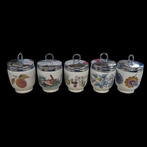 May include: A set of five white ceramic egg coddlers with shiny chrome lids featuring ring handles. Each coddler displays a unique botanical or bird illustration, including a peach, a small bird, blackberries, blue flowers, and orange floral patterns.