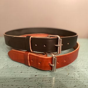 May include: Two leather belts with silver buckles. The top belt is black and the bottom belt is brown.