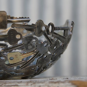Puede incluir: Un cuenco hecho completamente de llaves, con las llaves formando una forma esférica. El cuenco está hecho de metal y tiene un acabado plateado.