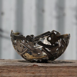Puede incluir: Un cuenco de plata hecho completamente de llaves. El cuenco está sobre una superficie de madera.