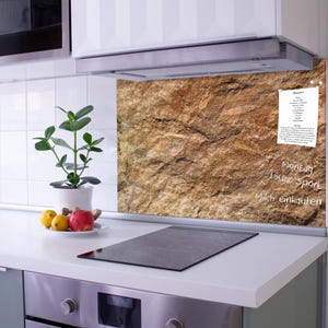 Può includere: Un pannello rettangolare per paraschizzi da cucina con una stampa ad alta risoluzione di una superficie rocciosa marrone testurizzata. Il pannello funge da bacheca magnetica, mostrando una ricetta appuntata e note scritte a mano.