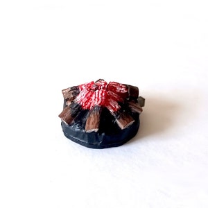 Può includere: Un falò in miniatura con fiamme rosse e arancioni e tronchi marroni su una base nera.