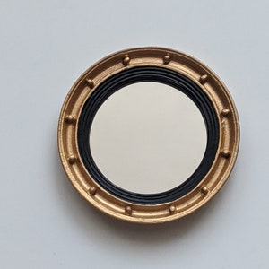 May include: A round mirror with a gold frame and black trim. The frame has a decorative pattern of small raised dots.