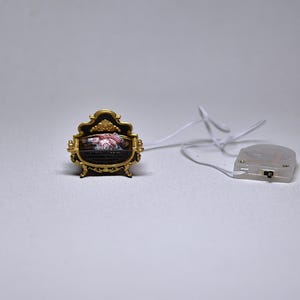 May include: A miniature fireplace with a gold frame and a black and red interior. The fireplace is lit up with a white cord and a battery pack.