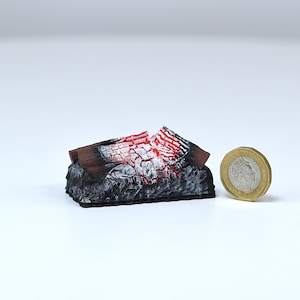 Könnte beinhalten: Ein Miniaturmodell eines Kamins mit einer realistischen Darstellung von brennenden Holzscheiten. Die Holzscheite sind in Rot-, Schwarz- und Weißtönen bemalt, um Flammen zu simulieren. Das Modell ist klein genug, um in die Handfläche zu passen.