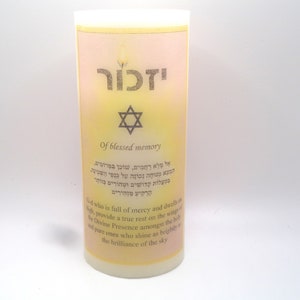 Op de afbeelding: Een witte kaars met een gele en roze ombre-ontwerp. De kaars heeft een Davidster en het Hebreeuwse woord "Yizkor" erop gedrukt. De tekst "Of blessed memory" is ook op de kaars gedrukt. De kaars is een gedenkkaars.