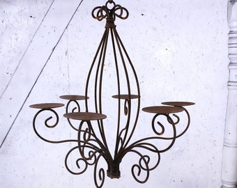 May include: A rustic, wrought iron candle chandelier with six candle holders. The chandelier has a decorative, scrolled design and is perfect for adding a touch of farmhouse charm to any room.