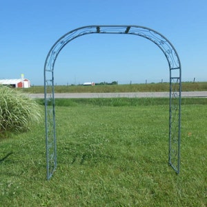 May include: A metal garden archway with a decorative design. The archway is made of black metal and has a curved top. It is standing in a grassy field.