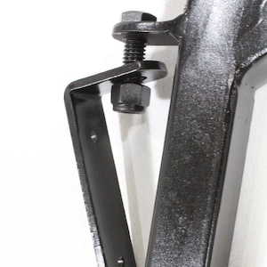 May include: Black metal bracket with a bolt and nut. The bracket is attached to a black metal pole.