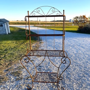 May include: A rusty metal plant stand with three shelves and decorative scrolls. The stand is made of wrought iron and has a rustic, vintage look.