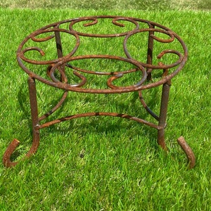 May include: A rusty metal plant stand with a circular top and three legs. The stand is made of twisted metal and has a rustic look.