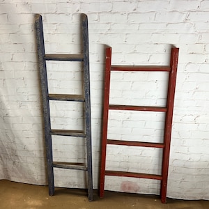 May include: Two wooden ladders, one painted blue and one painted red, standing against a white brick wall. Both ladders have four rungs.
