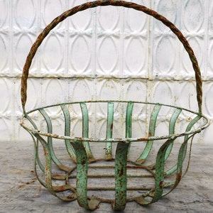 May include: An antique, distressed metal basket with a handle. The basket has a rounded shape with vertical bars and a handle. The metal has a weathered, aged appearance with a turquoise-green color and rust.