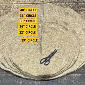 May include: A stack of beige circular mats with text indicating sizes from 19" to 40" diameter. A pair of black scissors with red accents rests on the mats. The mats are on a wooden surface.