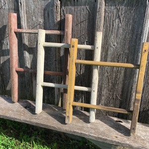May include: Three wooden ladders painted in different colors: red, white, and yellow. The ladders are leaning against a wooden wall.