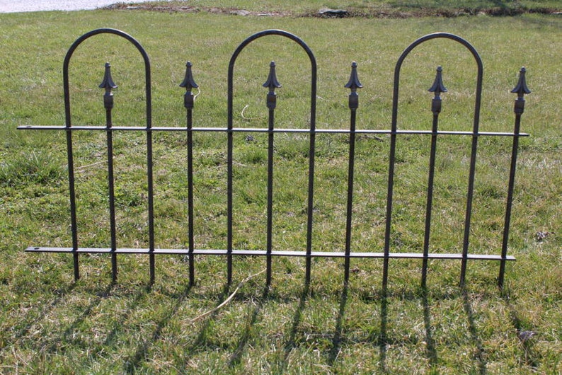 May include: Black metal fence with arched tops and decorative finials. The fence is in a grassy area.