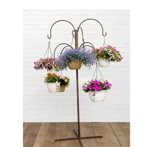 May include: A bronze-colored metal plant stand with a central pole and four curved arms, each holding a hanging basket. The baskets contain various colorful flowers including purple, pink, orange, and white blossoms in white and tan plastic pots.