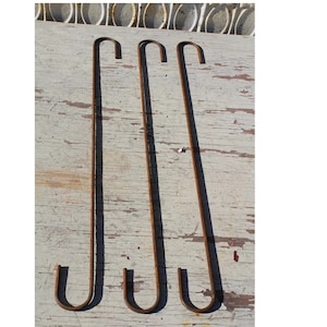 May include: Four rusty metal hooks, each with a rounded end, are arranged in a row on a white wooden surface.
