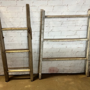 May include: Two rustic wooden ladders with three rungs each. The ladders are made of weathered wood and have a natural, distressed look. They are leaning against a white brick wall.