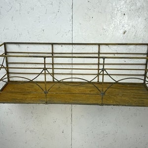 May include: Rectangular metal wall basket with a distressed gold finish. The basket features a wooden base and an openwork design with arched and geometric details. Ideal for displaying plants or decor.