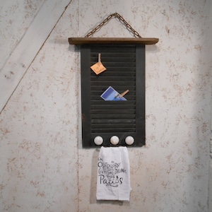 May include: A black wooden shutter with a white towel hanging below. The towel has the text "I'm Outdoorsy, I love getting drunk on patios". The shutter has a chain hanging from it and a few small white knobs.