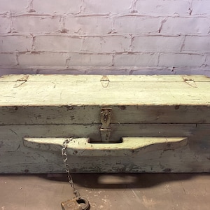 May include: A vintage wooden toolbox with a hinged lid, a metal latch, and a wooden handle. The toolbox is painted a light green color and has a chain and padlock attached.