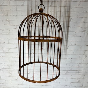May include: A large, rusty metal birdcage with a rounded top and a hanging hook. The cage is made of thin metal bars and has a simple, rustic design.