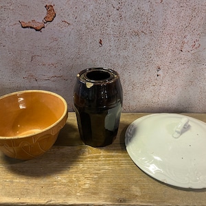 May include: Three vintage ceramic kitchenware items: a brown glazed bowl, a brown glazed jar with a lid, and a white glazed lid with a floral design.