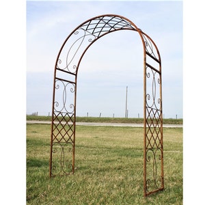 May include: A rusty metal archway with a decorative design. The archway is made of metal bars and has a lattice pattern. It is standing on a grassy field.