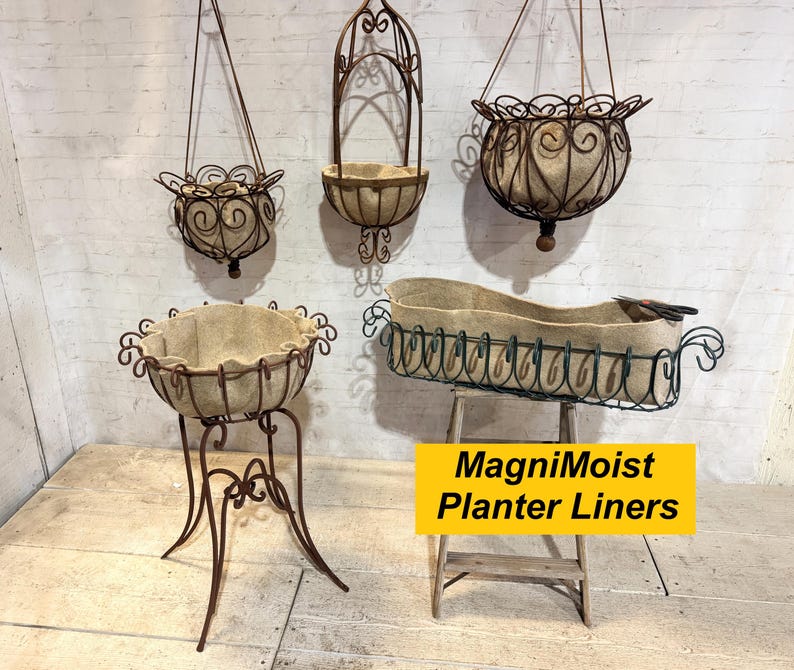 May include: A collection of brown metal planters with beige fabric liners, including three hanging baskets and two standing planters. A yellow rectangular sign with black text reads MagniMoist Planter Liners. The metal frames feature scrollwork.