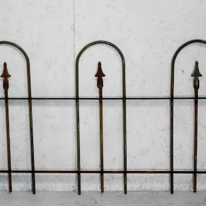 May include: A black metal fence with three arched sections and pointed finials. The fence is made of thin metal bars and has a rustic, aged look.