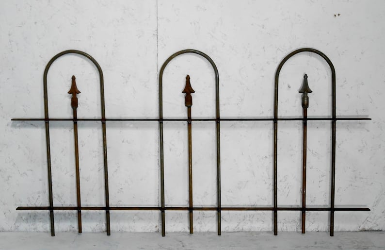 May include: A black metal fence with three arched sections and pointed finials. The fence is made of thin metal bars and has a rustic, aged look.