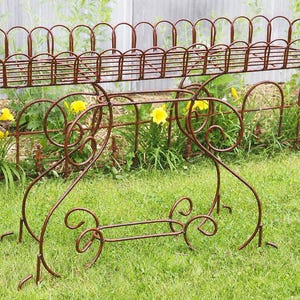May include: A brown metal plant stand featuring an elongated rectangular basket top with a curved wire railing. The base is constructed from arched metal supports with decorative scrollwork details and a central horizontal stabilizing bar.